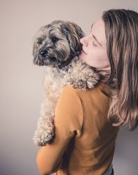 Woman carrying dog while standing against wall