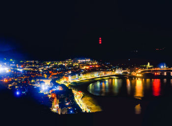 Illuminated buildings by river against sky in city at night