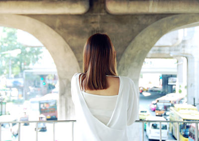 Rear view of young woman standing by railing under bridge