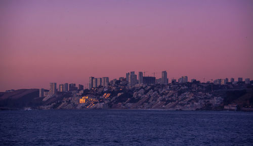 Scenic view of sea and buildings against sky at dusk