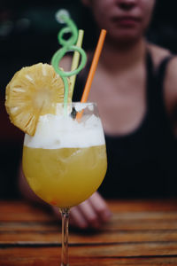 Close-up of cocktail in drinking glass on table with woman sitting in background