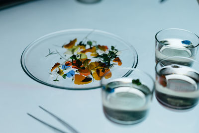 High angle view of flowers in plate by transparent glass on table
