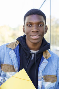 Smiling student with file leaning on wall