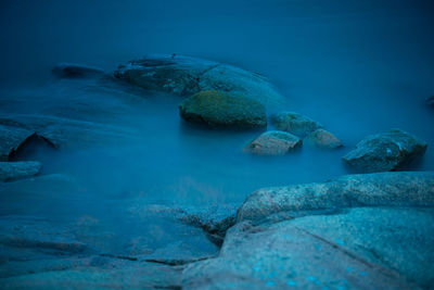 Long exposure night photo of waves washing over stones and cliffs
