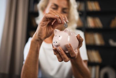 Midsection of woman putting coin in piggy bank