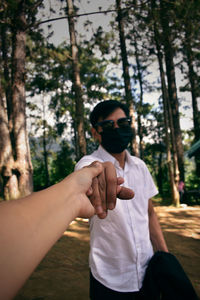 Young man wearing sunglasses standing against trees