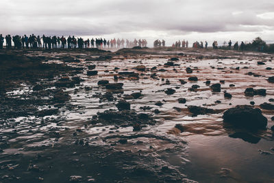 Distant view of people at geyser against sky