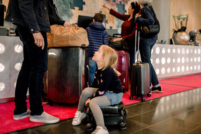 Girl sitting on suitcase while looking at father with family standing in background