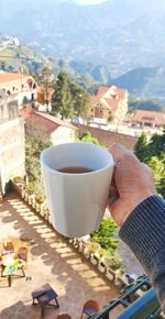 Close-up of hand holding coffee cup by buildings