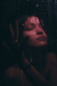 Close-up portrait of woman seen through wet glass window