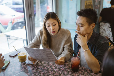 Male and female friends discussing while looking at menu card in restaurant