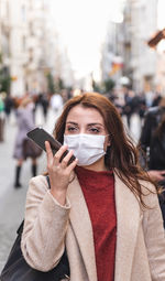 Portrait of young woman holding smart phone while standing on street