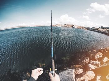 Cropped image of hands holding fishing rod at shore