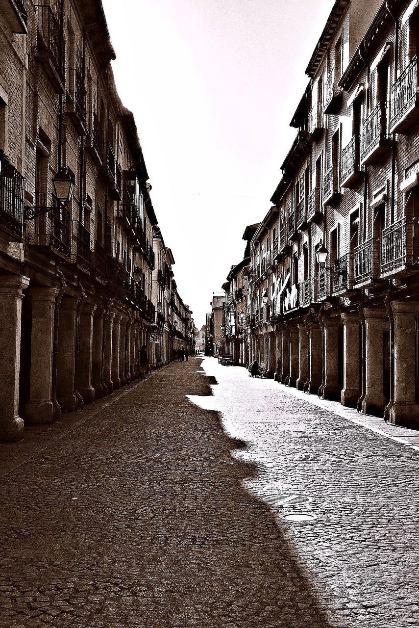 architecture, building exterior, the way forward, built structure, diminishing perspective, street, vanishing point, cobblestone, city, building, alley, incidental people, in a row, road, empty, history, travel destinations, clear sky, day, person