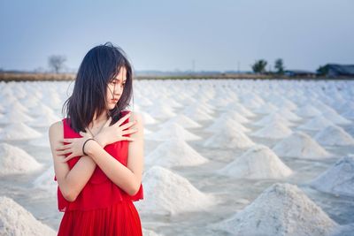A beautiful woman in a long red dress stands tall among salt fields and blue skies.