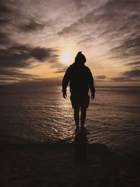 Rear view of silhouette man standing at beach during sunset