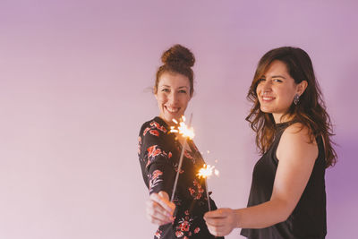 Portrait of women holding illuminated sparklers against wall