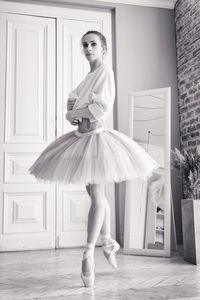 Charming ballerina poses showing her legs in the room in front of the mirror in pointes and tutu