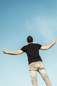 Rear view of man with arms outstretched against blue sky