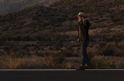 Adult man in cowboy hat hitchhiking on roadside on desert during sunset. almeria, spain