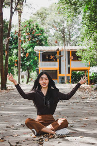 Portrait of smiling young woman throwing leaves while sitting on road in forest