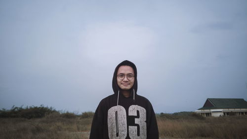 Portrait of smiling young woman standing on field against sky