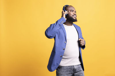 Portrait of young man standing against yellow background