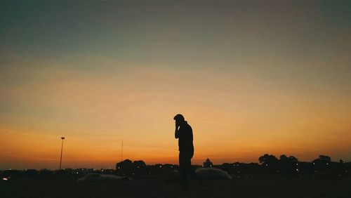 Silhouette man using phone against orange sky during sunset