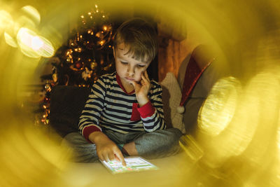 Boy using digital tablet while sitting on sofa at home during christmas