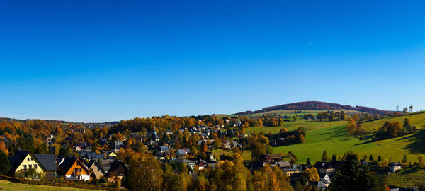 Panoramic view of trees and houses against clear blue sky