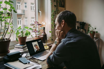 Male entrepreneur discussing with colleague on video call through laptop at home during covid-19