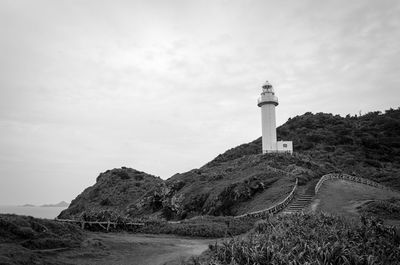 Lighthouse on cliff by sea against sky