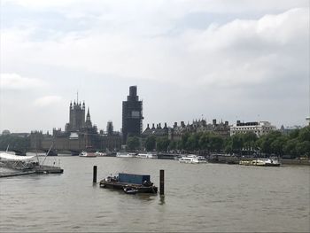 Sailboats in river by buildings against sky