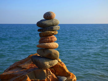 Stack of stones on rock by sea against clear sky