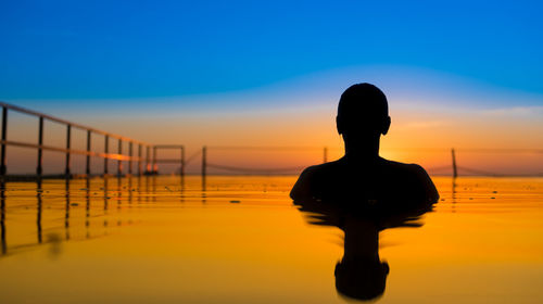 Silhouette person in sea against dramatic sky during sunset