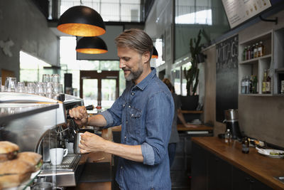 Smiling barista steaming milk in cafe