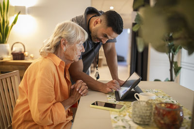 Male nurse assisting senior woman in using digital tablet at nursing home