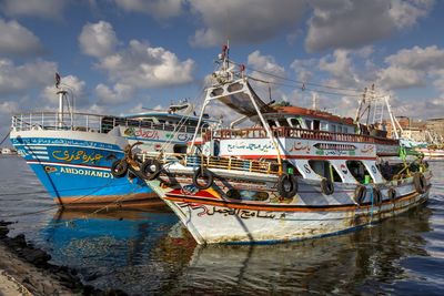 Fishing boats moored at harbor against sky