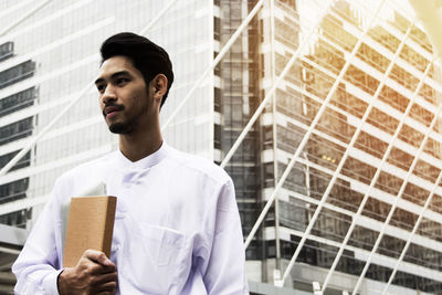 Businessman holding book while standing in city