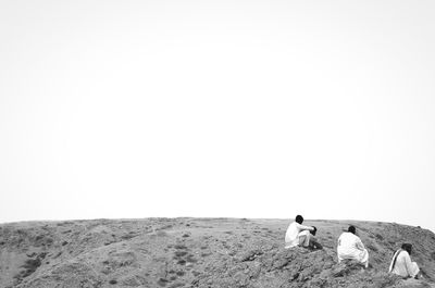 People resting on field against clear sky