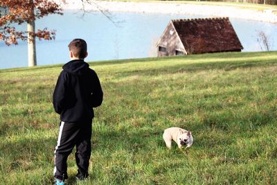 Rear view of boy with dog on grassy field