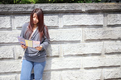 Mid adult woman reading book while standing against wall
