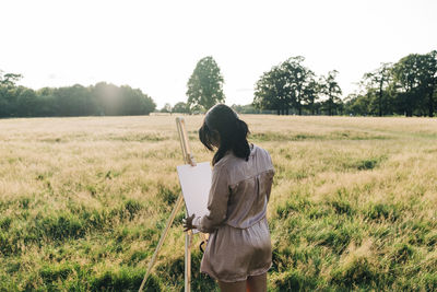 Woman painting on canvas while standing at park