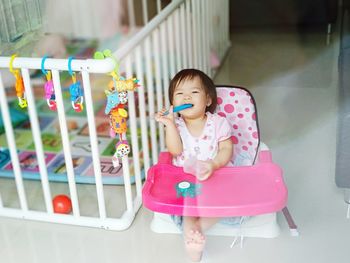Cute girl sitting on high chair by crib at home