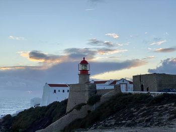Lighthouse amidst buildings by sea against sky