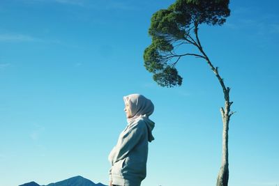 Side view of young woman standing against clear blue sky