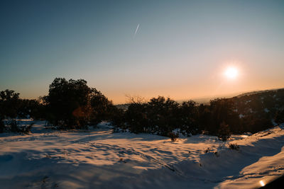 Snow covered landscape against sky during sunset