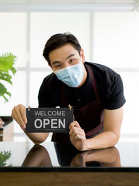 Portrait of man wearing mask holding sign board at cafe