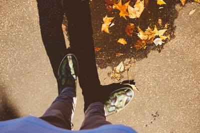 Low section of man standing by autumn leaves on road during sunny day