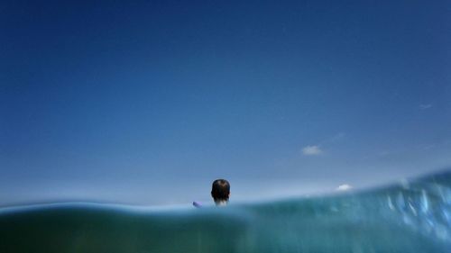 Rear view of man swimming in sea against blue sky